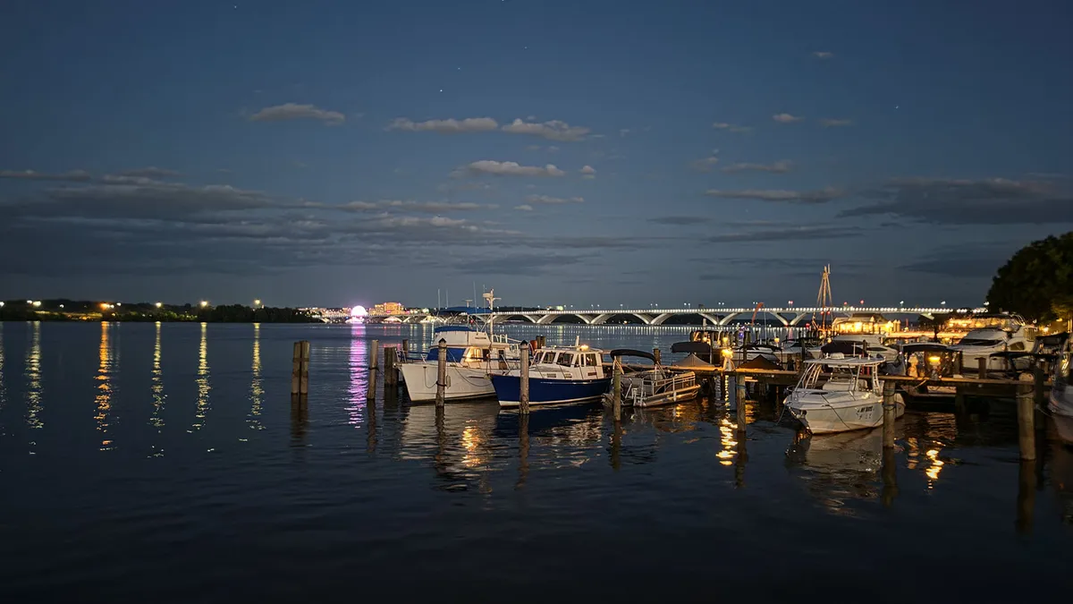 late evening view of boats at a dock, in the distance a bridge and ferris wheel lines the far shore