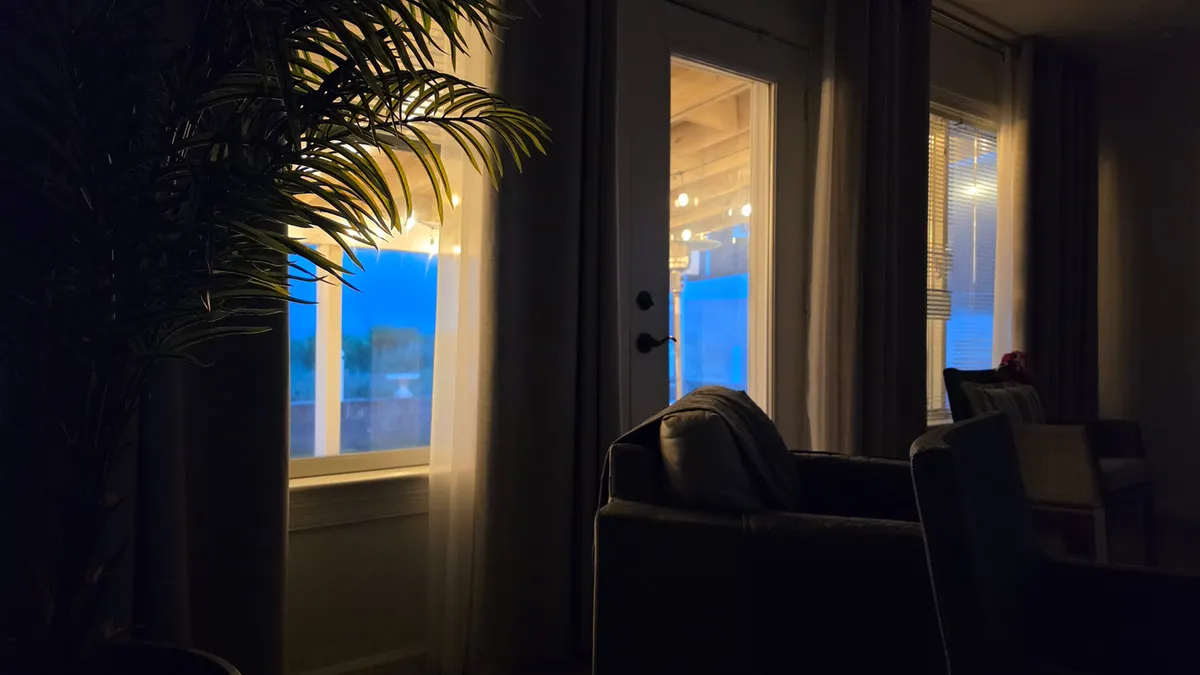 large bulb string lights glow through a window from a dark living room with couch and plant inside