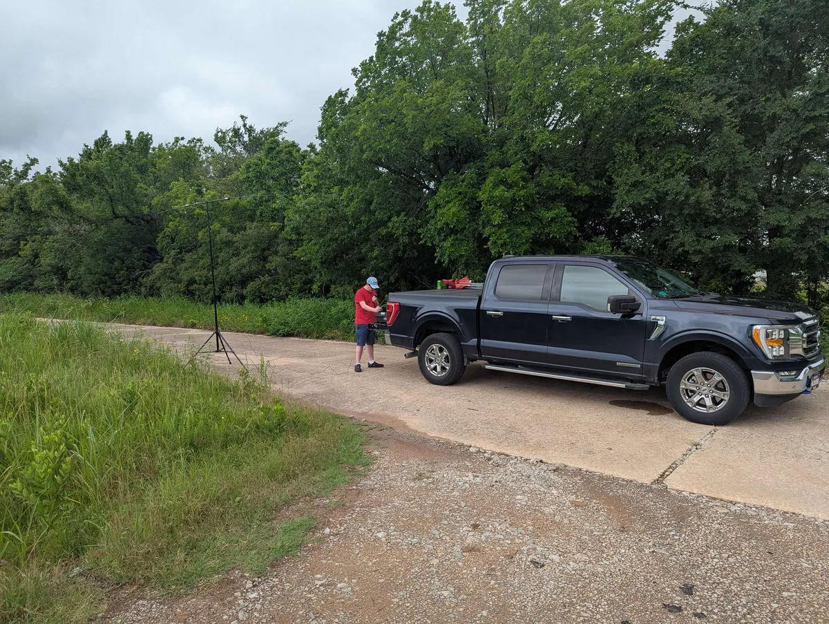 WW0CJ operating a radio from the tailgate of a truck, with a buddipole antenna to his side.