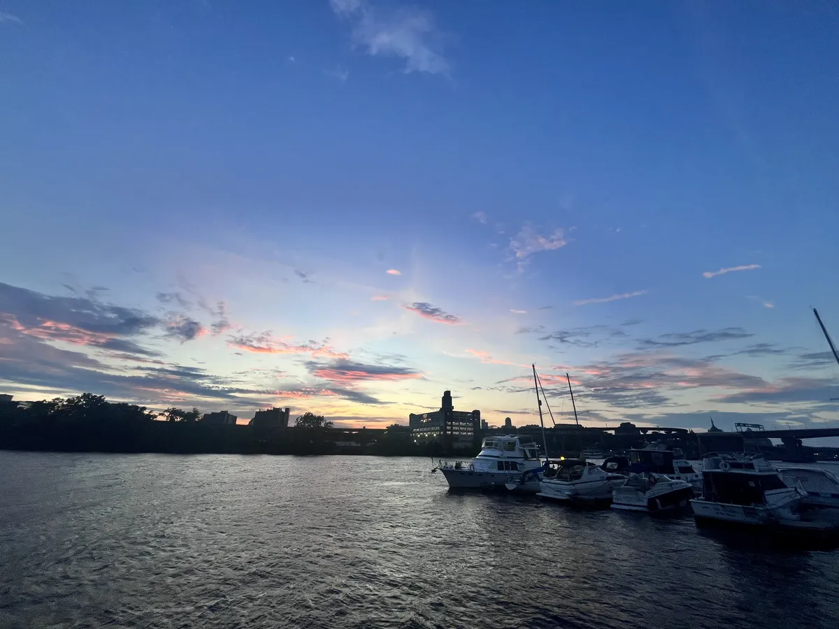 Looking at a sunset over Albany from across the Hudson River. There aren't very many clouds in the sky, but each one is dark gray and lined with a vivid coral red. The sky itself is a beautiful gradient from deep blue to pale gold.