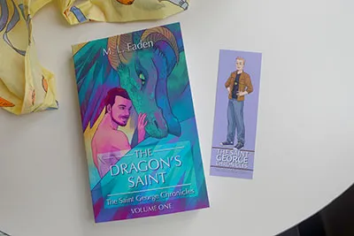 A book cover showing a brunette man with a dragon and a bookmark with a blonde man.