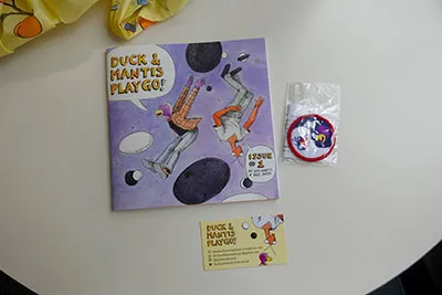 A square zine showing an illustrated Duck and Preying Mantis floating beside Go stones.