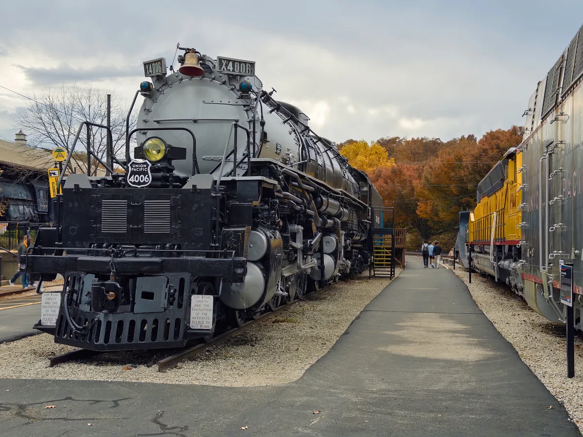 Two Union Pacific engines, including Big Boy #4006, frame warm autumn leaves between them.