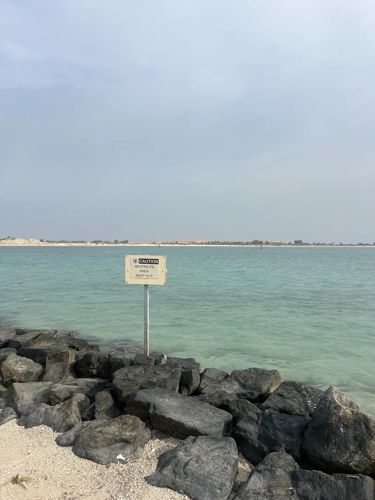 Big rocks on the beach with a 'Caution: Restricte Area Keep Out' sign