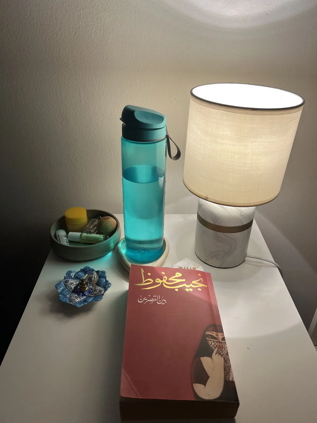 Nightstand with a lamp, a copy of Palace Walk, an incense holder and various ointments